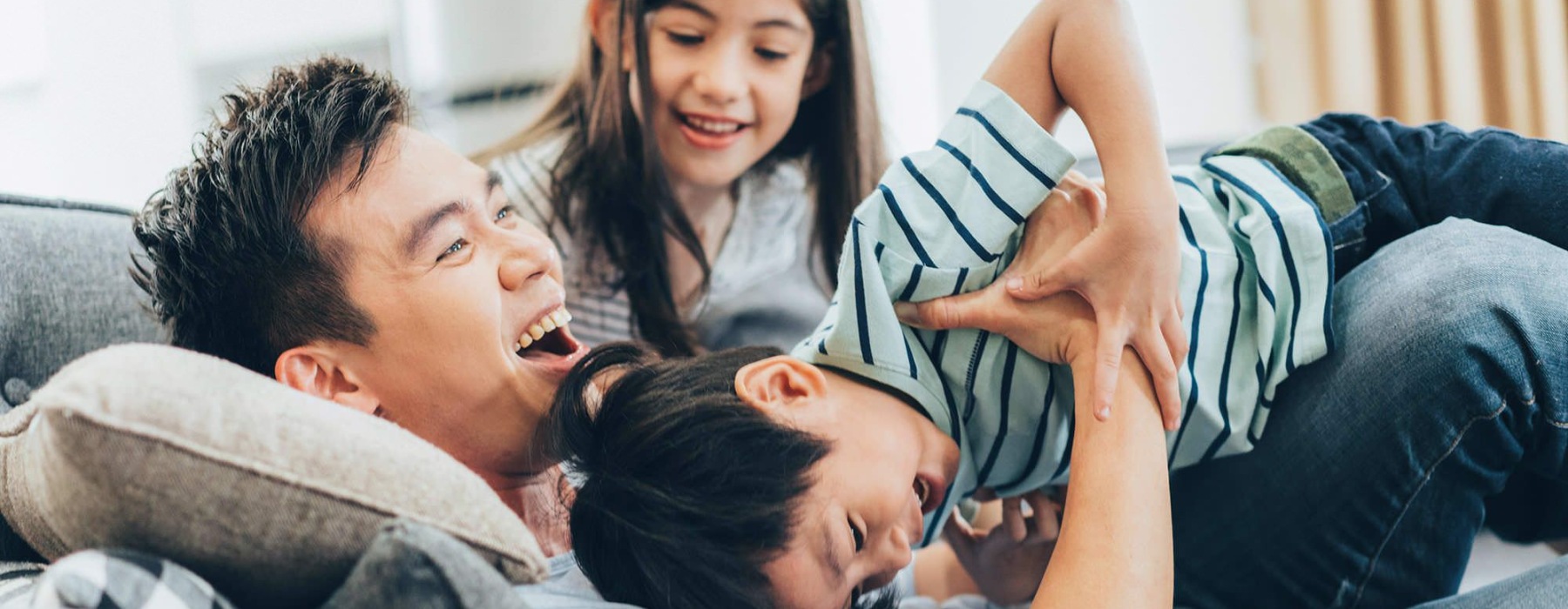 father plays on a couch with his young children